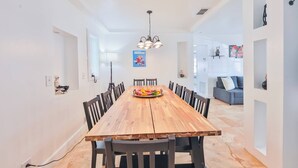 A dining area with a wooden table and chairs, a chandelier, and a sofa in the background.
