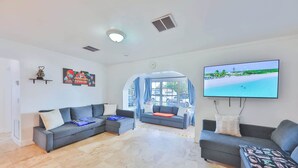 A spacious living room with two grey sofas, a flat-screen TV, and a large window with a view of a beach.