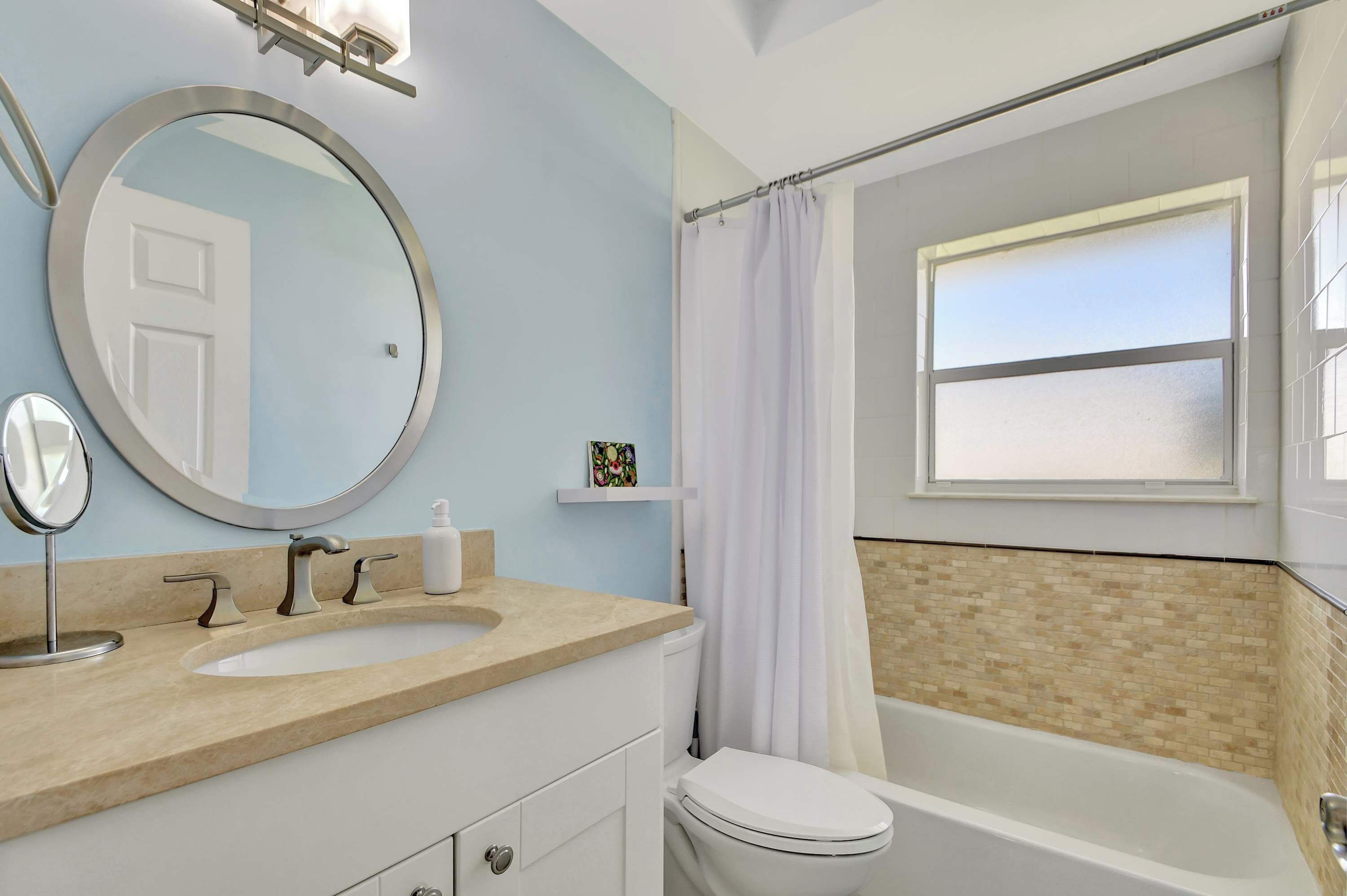 Un bagno con uno specchio rotondo, un lavandino, un water e una vasca da bagno.