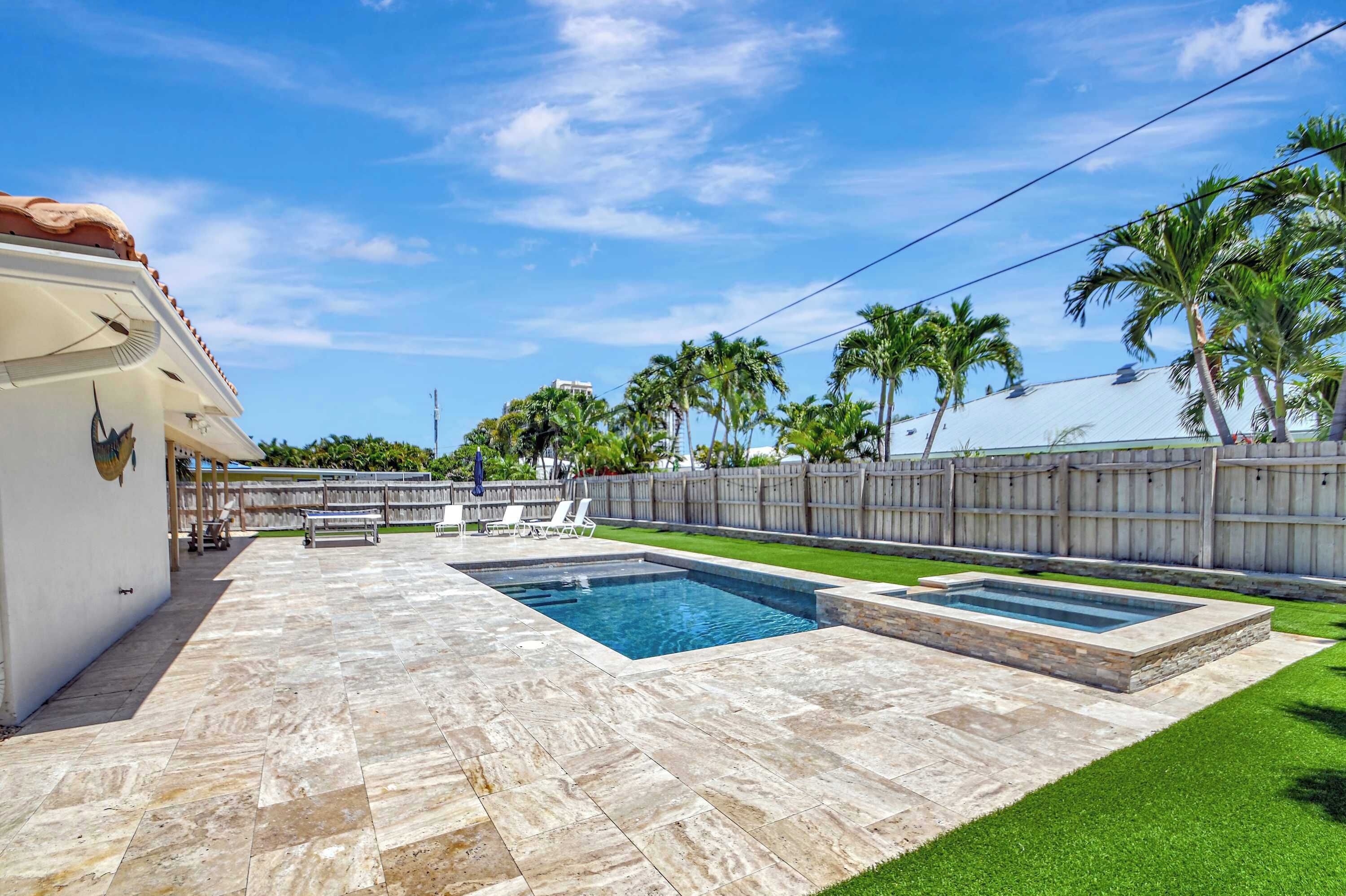 A backyard with a swimming pool, a covered patio, and a wooden fence.