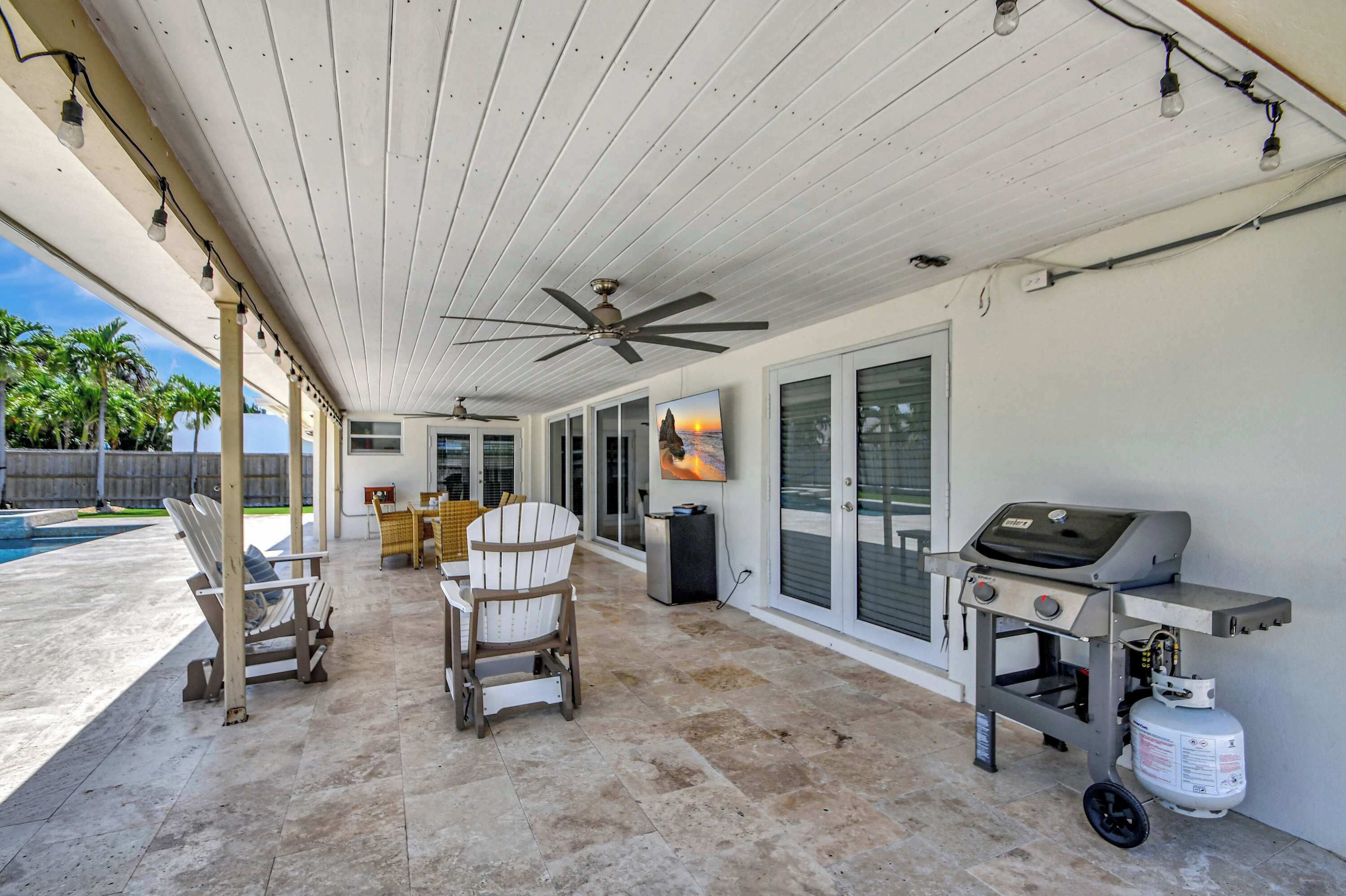 A covered patio with ceiling fans, outdoor seating, a barbecue grill, and a pool.