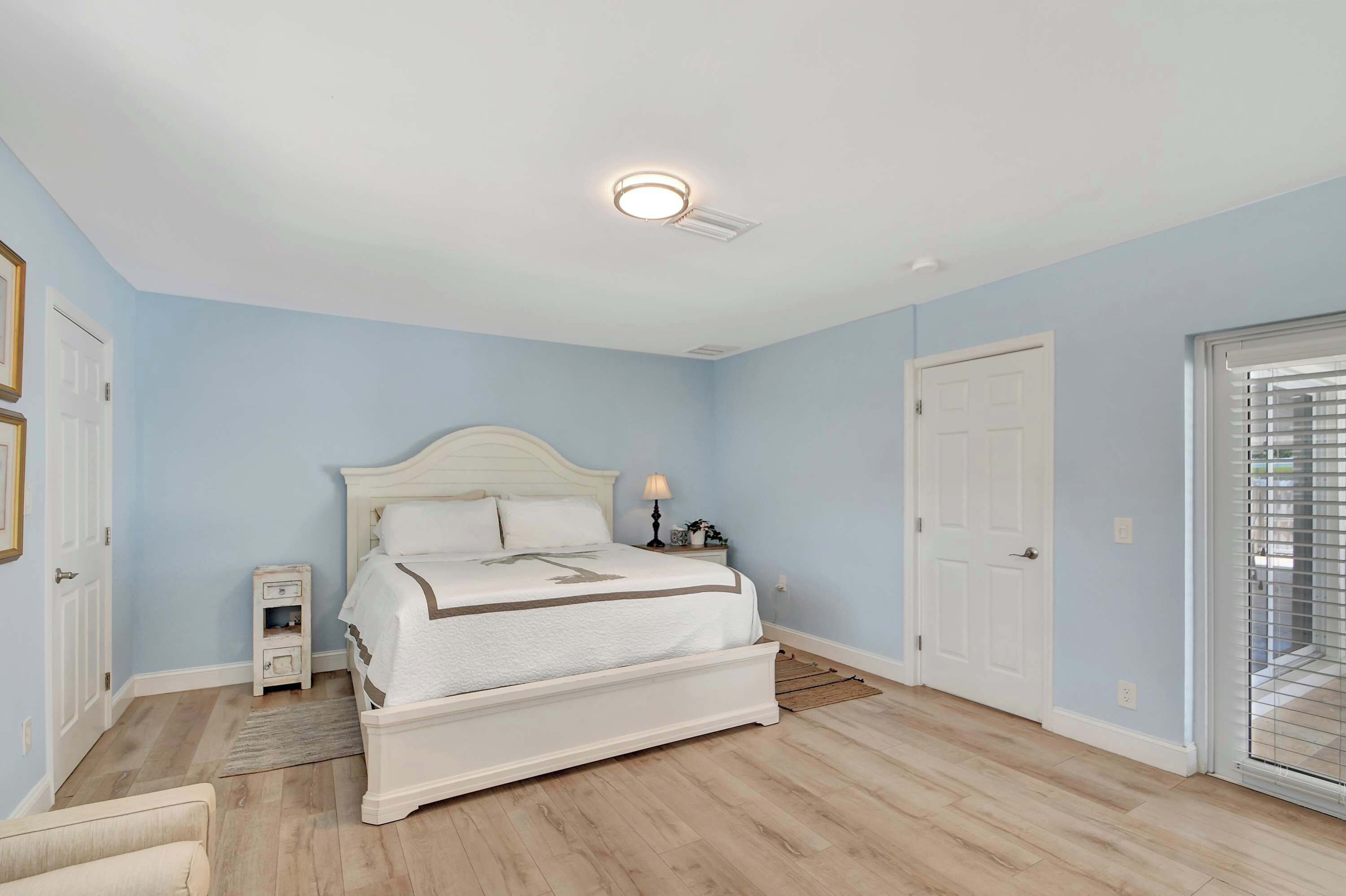A bedroom with a white bed, a nightstand, a lamp, and a door.