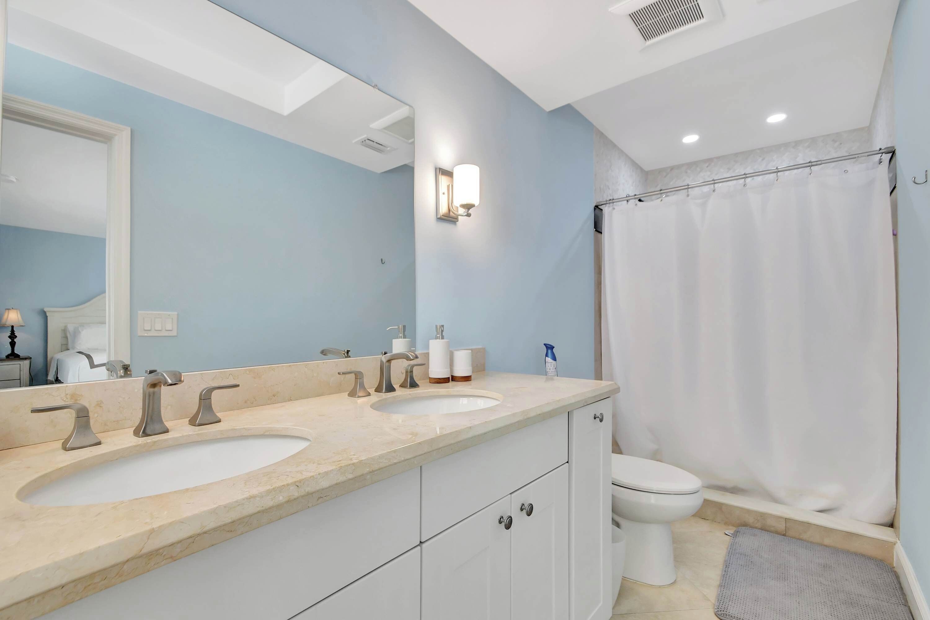 A bathroom with two sinks, a toilet, a shower curtain, and a mirror.