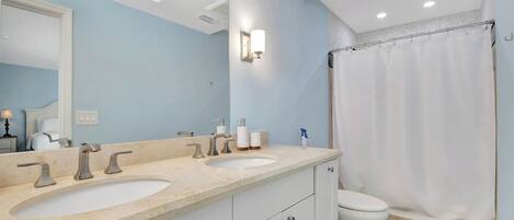 A bathroom with two sinks, a toilet, a shower curtain, and a mirror.