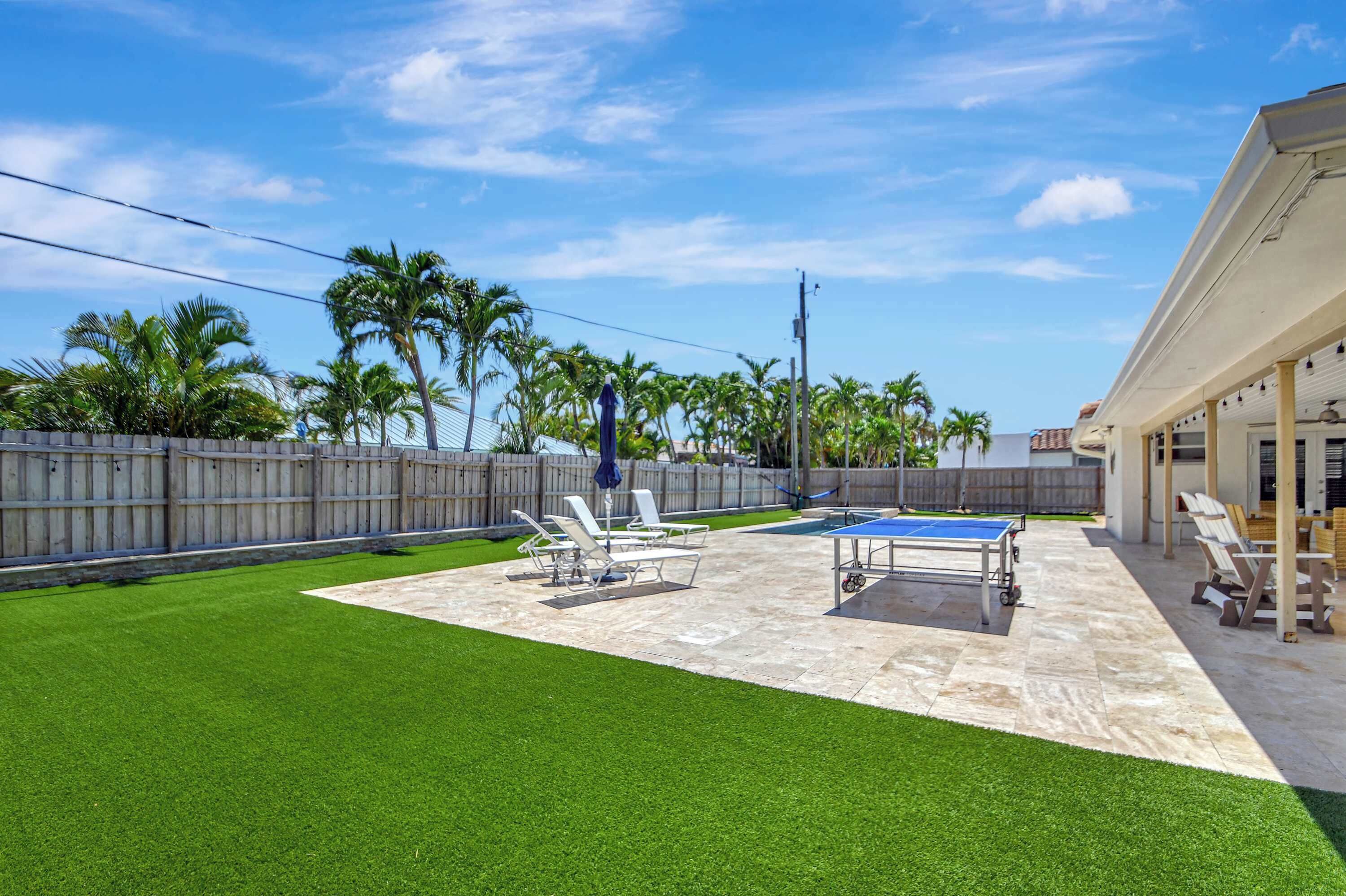 A backyard with artificial grass, a ping pong table, and lounge chairs.