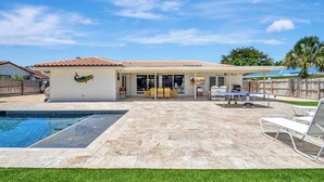 A backyard with a swimming pool, patio furniture, and a covered seating area.