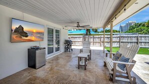 A covered patio area with a ceiling fan, outdoor seating, a TV mounted on the wall, and a view of the ocean.