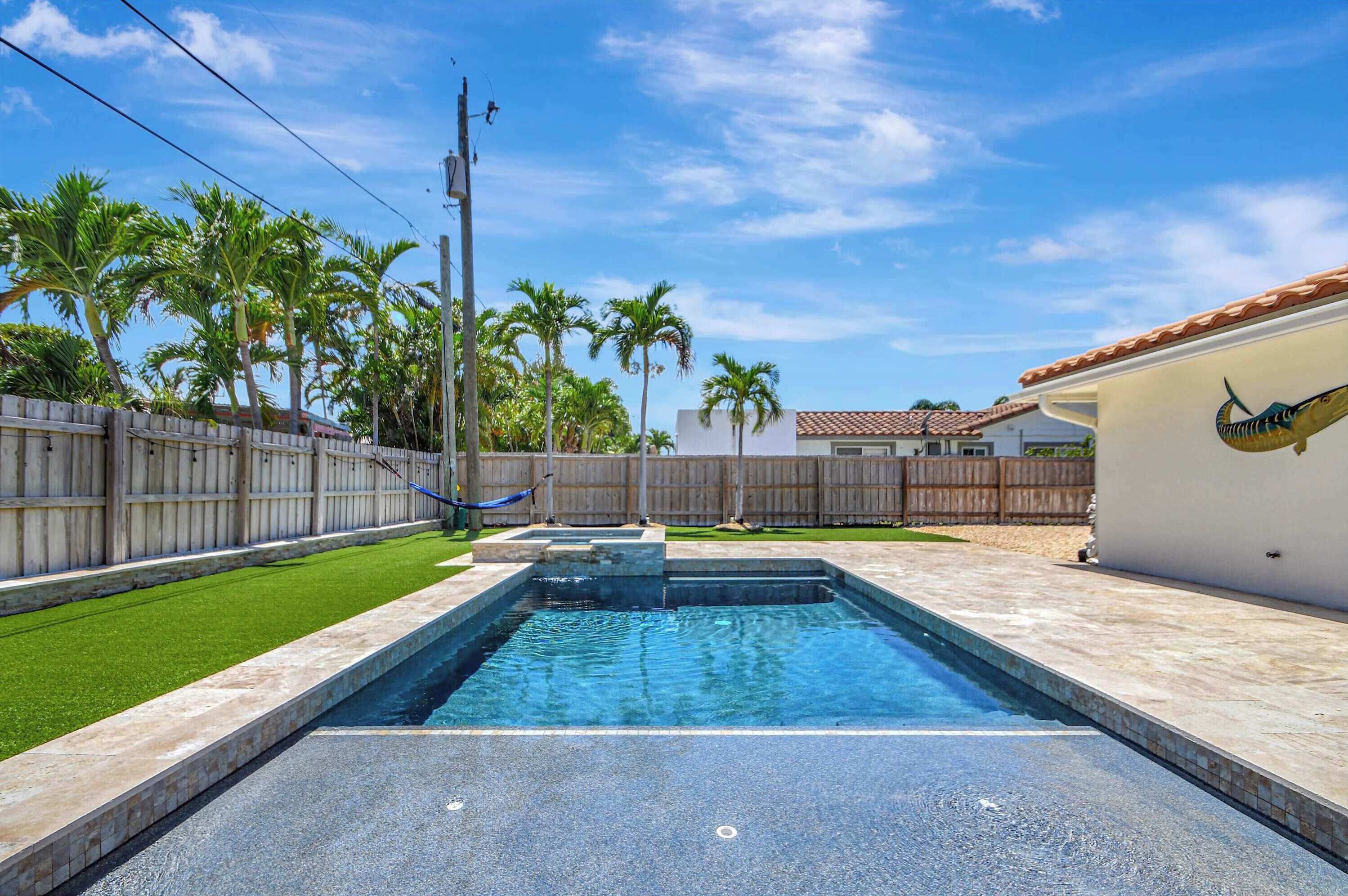 A swimming pool with a wooden fence, palm trees, and a hammock.