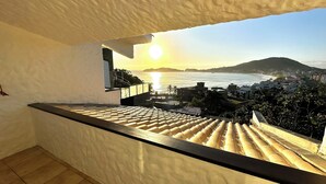 Varanda com vista para o mar e uma montanha distante ao pôr do sol.