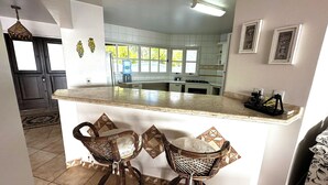 A kitchen with a central island, two wicker chairs, and a water dispenser. - SANTORINI HOUSE - HEATED POOL - 4BEDROOM - 140MT FROM BOMBINHAS BEACH, (Centro Bombinhas)