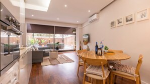A modern kitchen with a built-in oven, a dining area with a wooden table and chairs, and a large window overlooking a garden. - Saldanha Terrace by LovelyStay (Lisboa)