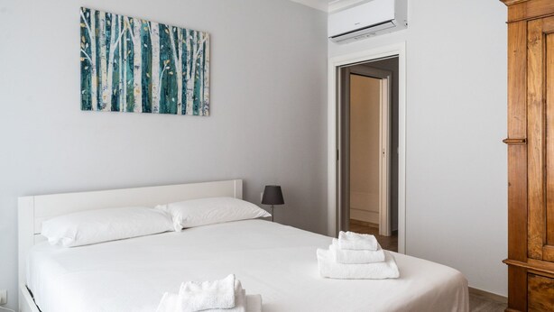 A hotel room with a large bed, white bedding, a wooden wardrobe, and a painting on the wall.