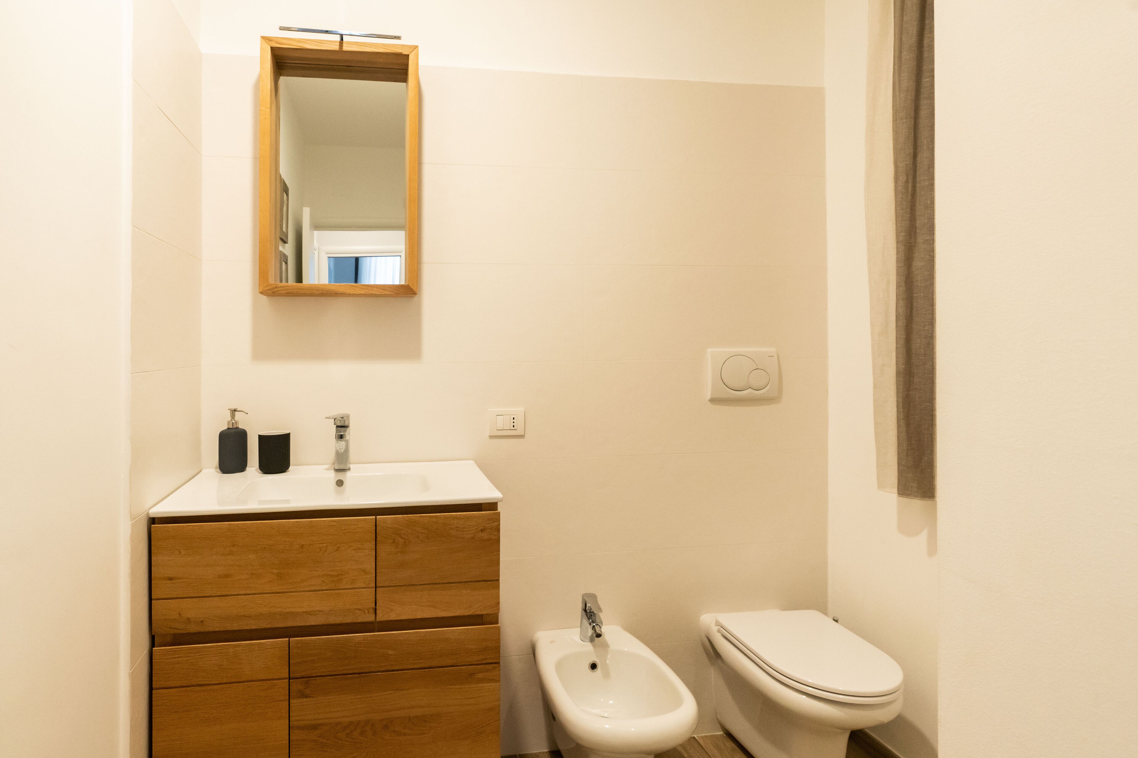 Ein kleines Badezimmer mit einem Holzbadezimmer-Möbel, einem weißen Waschbecken, einem Bidet und einer Toilette.