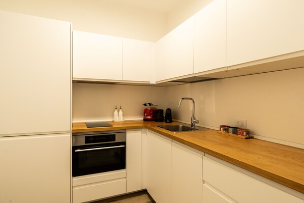 A compact kitchen with white cabinets, a wooden countertop, a built-in oven, a sink, and a coffee maker. - Appartamento Adara by Wonderful Italy (Bari)