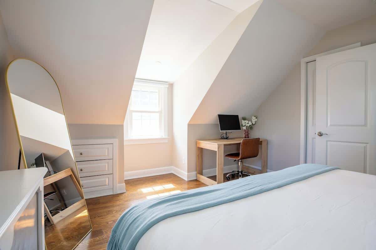 Une chambre à coucher avec un lit, un bureau avec un ordinateur, une chaise, une armoire et une fenêtre.