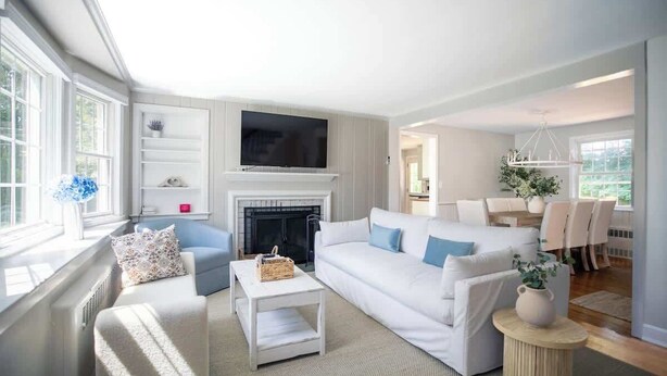 A modern living room with a fireplace, a television, and a dining area with chairs and a table. - Family Cottage with 4 King Beds and Fire Pit, Norwalk/Westport Border (Norwalk)