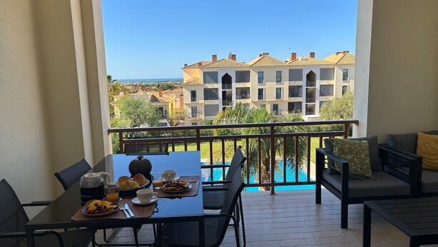 En balkon med et spisebord dækket til morgenmad, en pool og udsigt til en boligbygning.