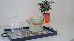 Un verre à vin transparent, une théière verte avec un manche en bois et une plante en pot rouge, le tout posé sur un plateau.