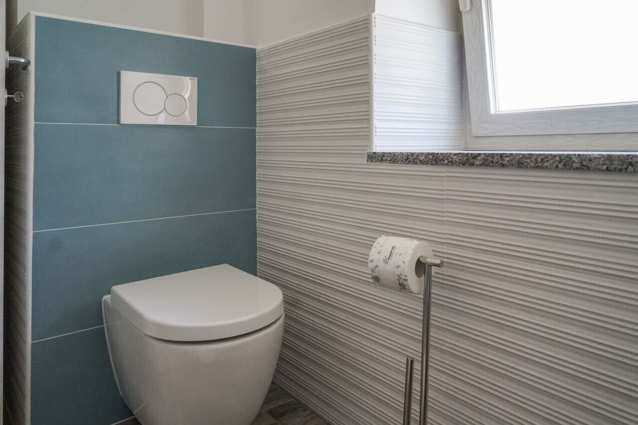 Et badeværelse med toilet, et håndklæderør med toiletpapir og en luftfrisker monteret på væggen.