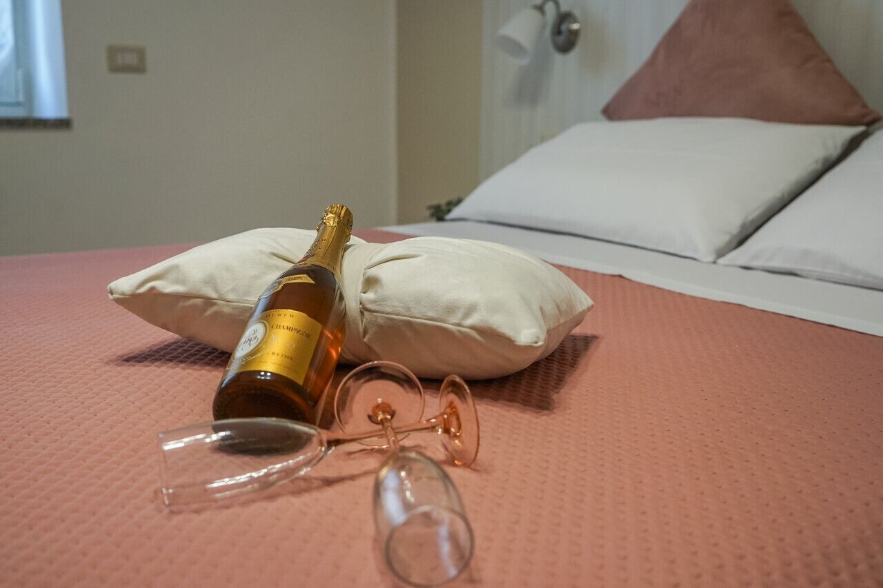 Ein Bett mit einer Champagnerflasche und zwei Weingläsern auf einer rosa, strukturierten Tagesdecke.