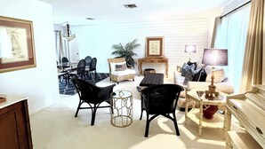 A spacious living room with a dining area, featuring wicker furniture, a fireplace, and a large window with curtains. - Beautiful Naples home, walk to private beach! (Naples)