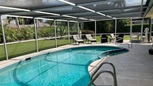 A swimming pool with a glass enclosure, surrounded by lounge chairs and a patio area. - Beautiful Naples home, walk to private beach! (Naples)