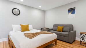 Une chambre à coucher moderne avec un lit, un canapé, une petite table et une affiche accrochée au mur.