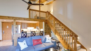 Un'ampia zona giorno con un divano blu, una scala in legno e una cucina sullo sfondo.