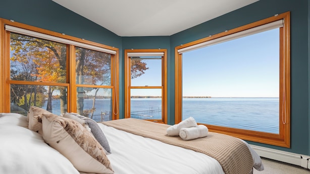 Ein Schlafzimmer mit großem Fenster und Blick auf einen See und Bäume.