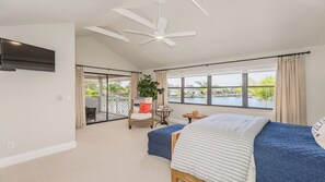 Un dormitorio con cama, ventilador de techo, vista a un cuerpo de agua y balcón con silla y planta.