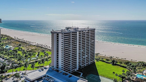 A high-rise hotel with a rooftop pool, a beach view, and a parking area with cars. - Escape to paradise at our beachfront condo at the Gulfview. (Marco Island)