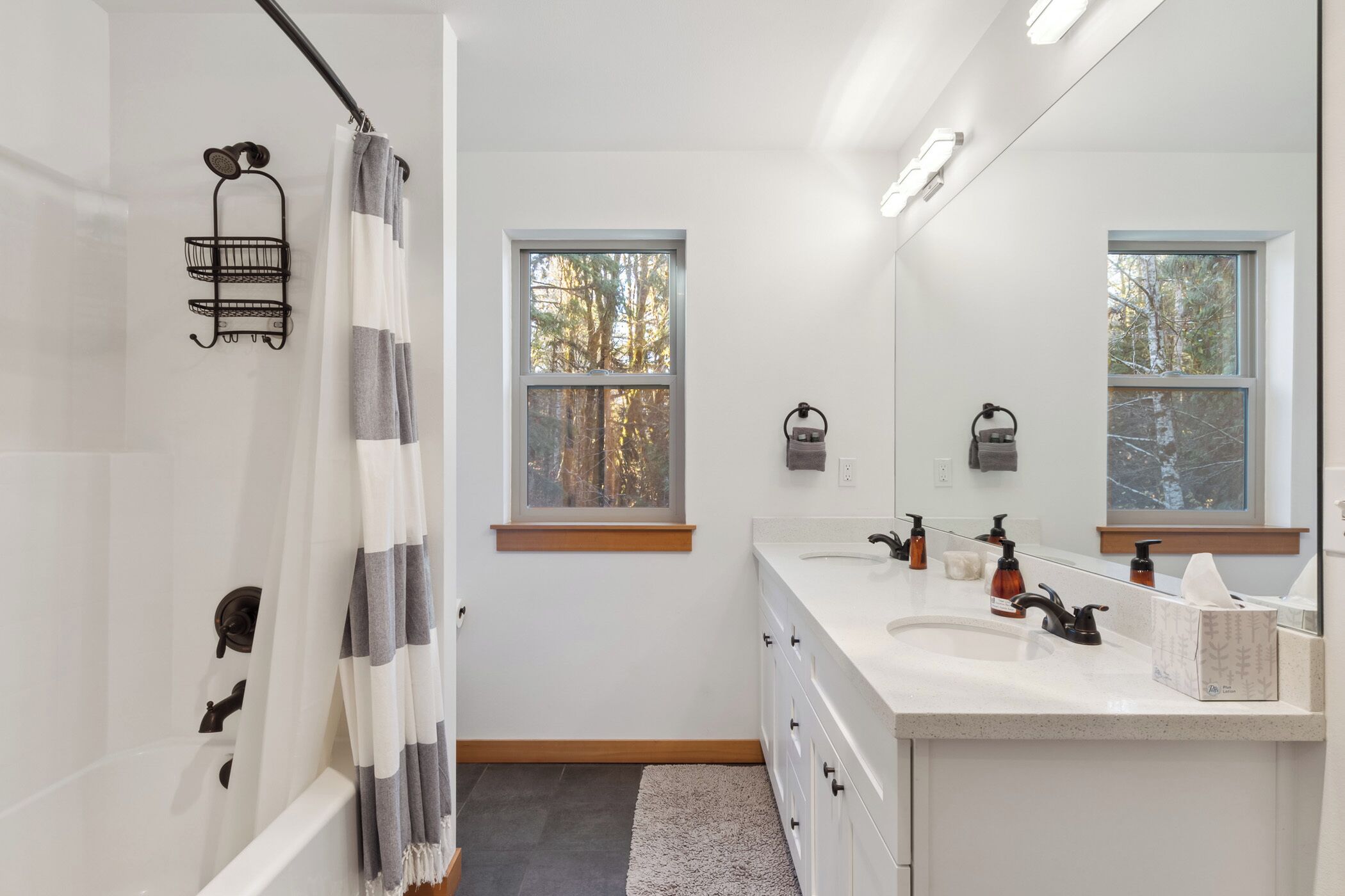 A modern bathroom with a bathtub, a large mirror, a vanity with a sink, and two windows providing natural light.