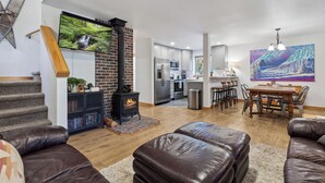 Una sala de estar moderna con chimenea, sofás de cuero, comedor y cocina al fondo.