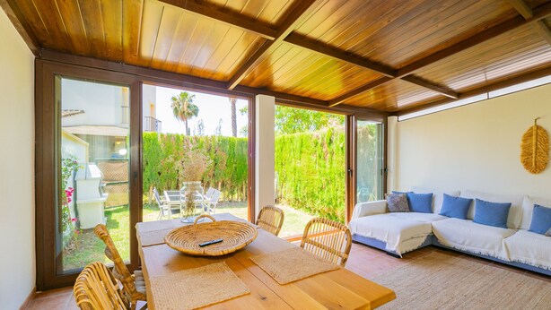 A dining area with a wooden table, wicker chairs, and a glass door leading to a garden. - Cubo's Townhouse Sierrezuela / communal pool / BBQ / terrace / parking (Mijas Costa)