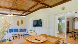 A cozy living area with a wooden ceiling, a sofa with blue cushions, a TV mounted on the wall, and a dining table with woven placemats and chairs. - Cubo's Townhouse Sierrezuela / communal pool / BBQ / terrace / parking (Mijas Costa)