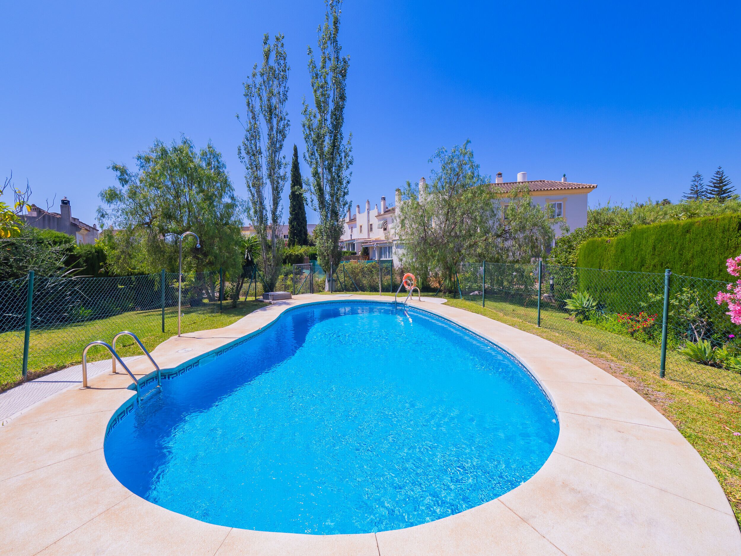 A swimming pool with a curved edge, surrounded by a fence and greenery.