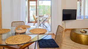 A dining area with a glass table, wicker chairs, and a TV mounted on the wall. - Cubo's Townhouse Sierrezuela / communal pool / BBQ / terrace / parking (Mijas Costa)