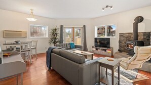 Un salon moderne avec un canapé gris, un téléviseur, une cheminée et un coin repas comprenant une table et des chaises.