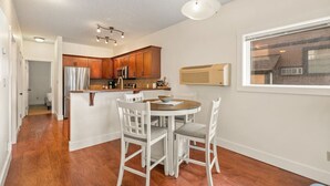 Une cuisine moderne avec des meubles en bois, des appareils en acier inoxydable et un coin repas doté de chaises blanches.