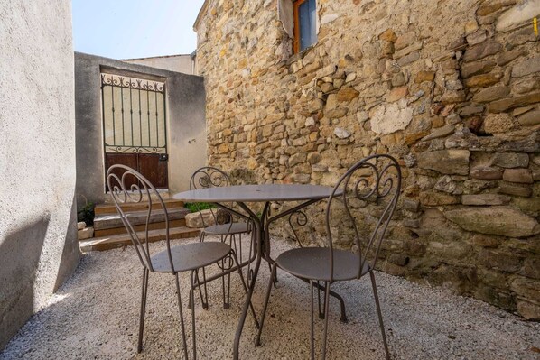 Un edificio de piedra con una verja de metal, una mesa con sillas y una pequeña escalera que lleva a una puerta.