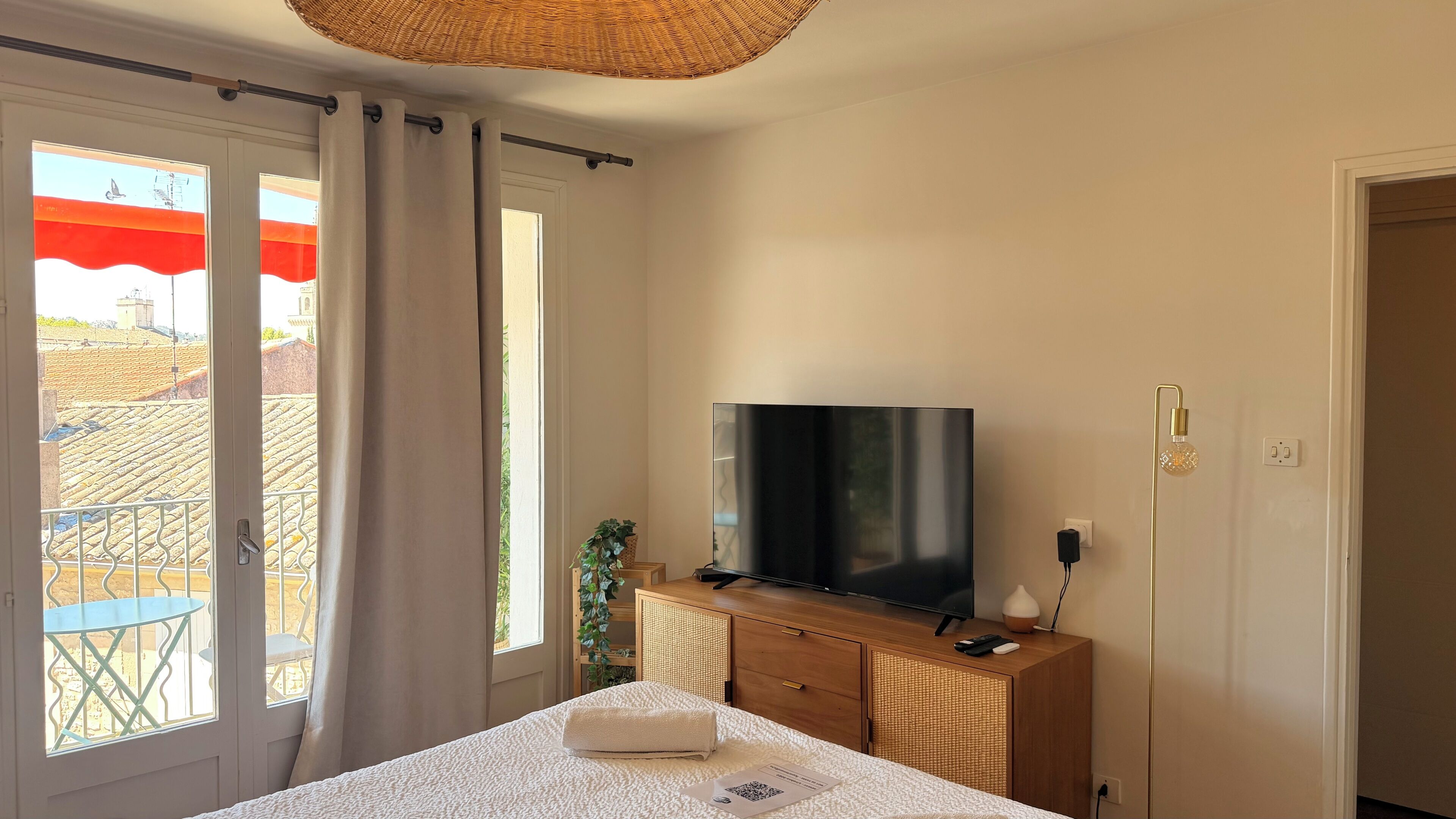 Hotellihuone, jossa on sänky, televisio, puinen lipasto ja parveke, jolta on näkymä.