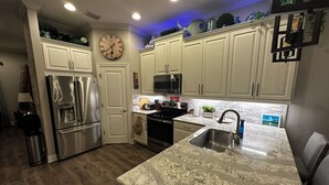 Una cocina moderna con armarios blancos, electrodomésticos de acero inoxidable, encimera de granito y un reloj en la pared.