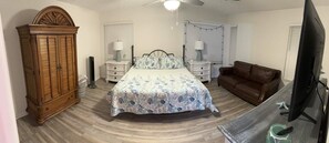 Um quarto com uma cama, um guarda-roupa de madeira, um sofá de couro marrom e uma televisão.