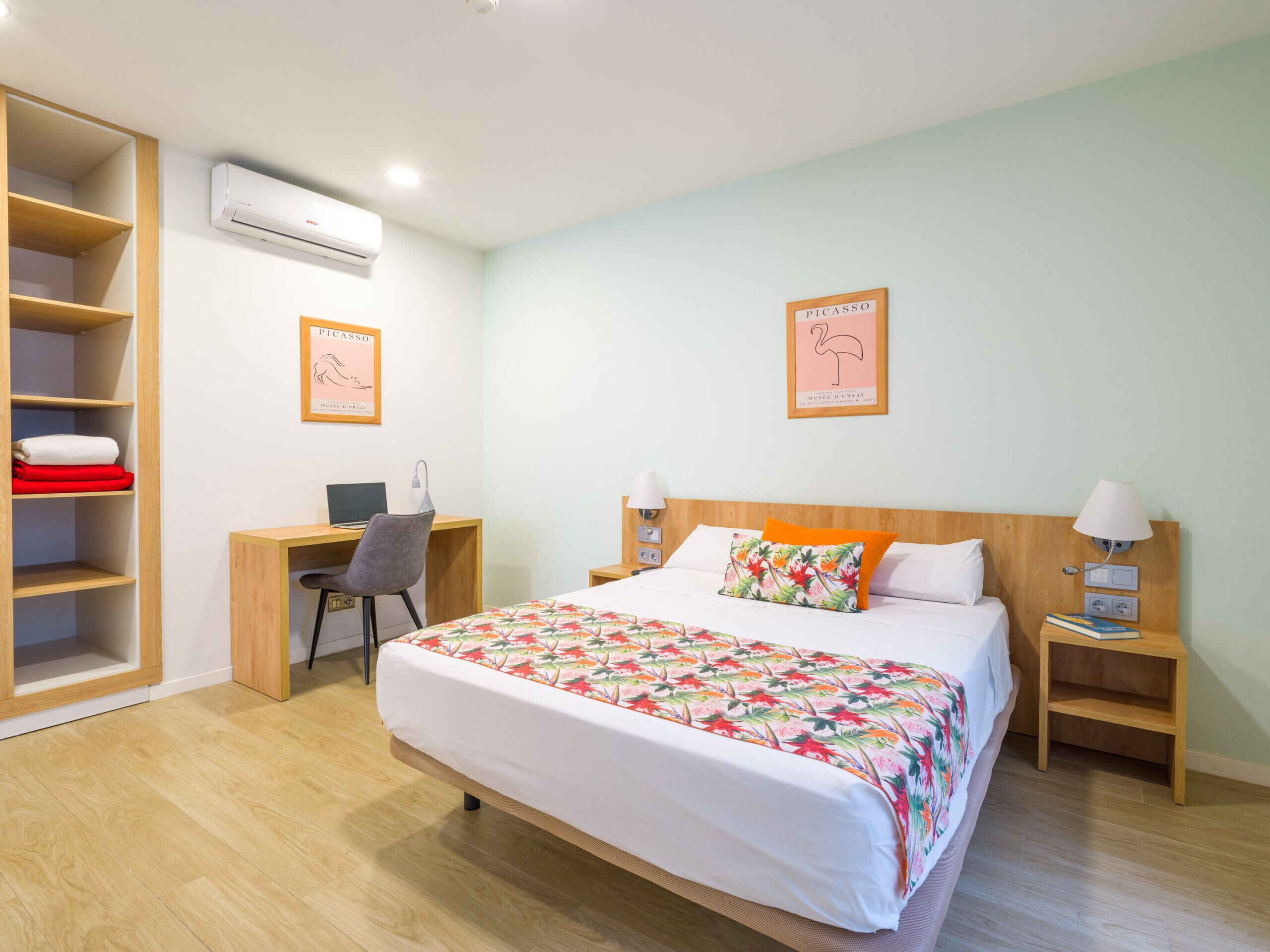 A hotel room with a bed, a desk, a chair, an air conditioner, and a wardrobe.