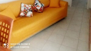 Ein Wohnzimmer mit einer Couch, Kissen, einer Wandleuchte und einer Tür zu einem anderen Raum.