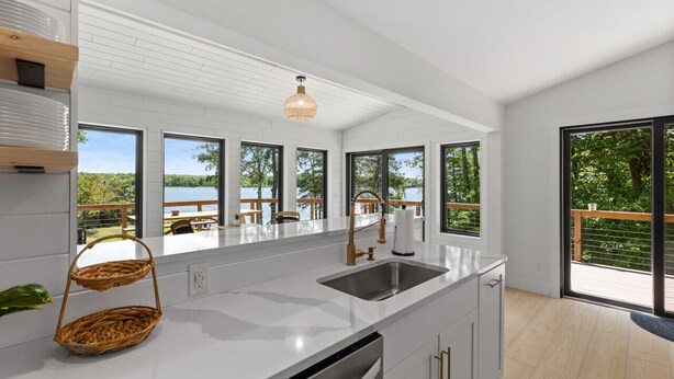 A modern kitchen with a large island, white cabinetry, and a view of a deck and trees. - Lake House w/Hot Tub, Game Room, Fireplace & Beach (Crosby)