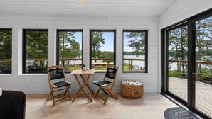 A room with large windows, a wooden table, two chairs, and a wicker basket. - Lake House w/Hot Tub, Game Room, Fireplace & Beach (Crosby)