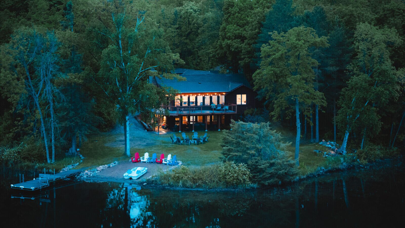 A lodge with a deck, outdoor seating, and a dock with a boat.