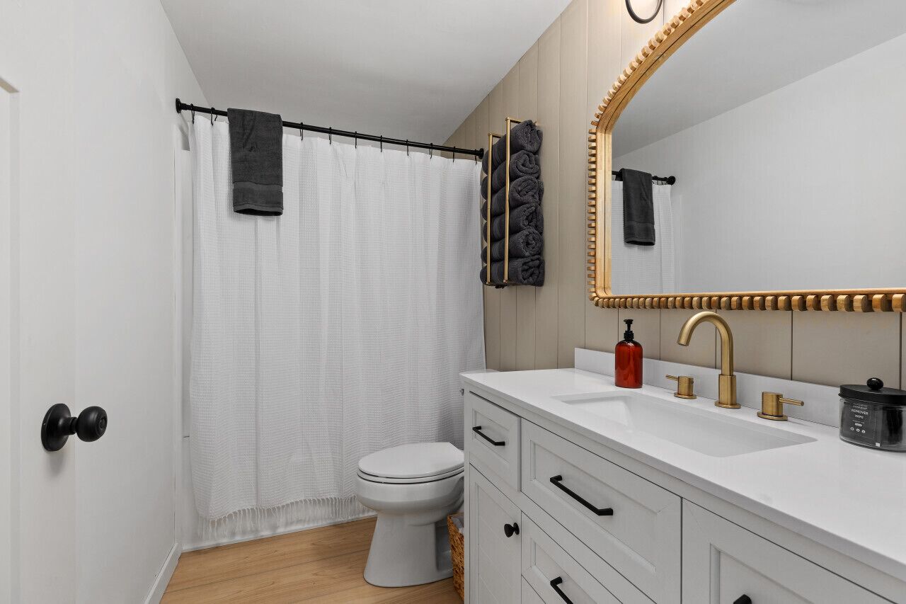A bathroom with a white toilet, a white sink with gold fixtures, and a large mirror with a gold frame.
