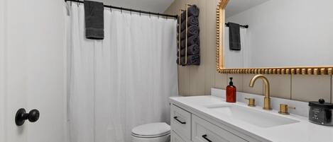 A bathroom with a white toilet, a white sink with gold fixtures, and a large mirror with a gold frame.